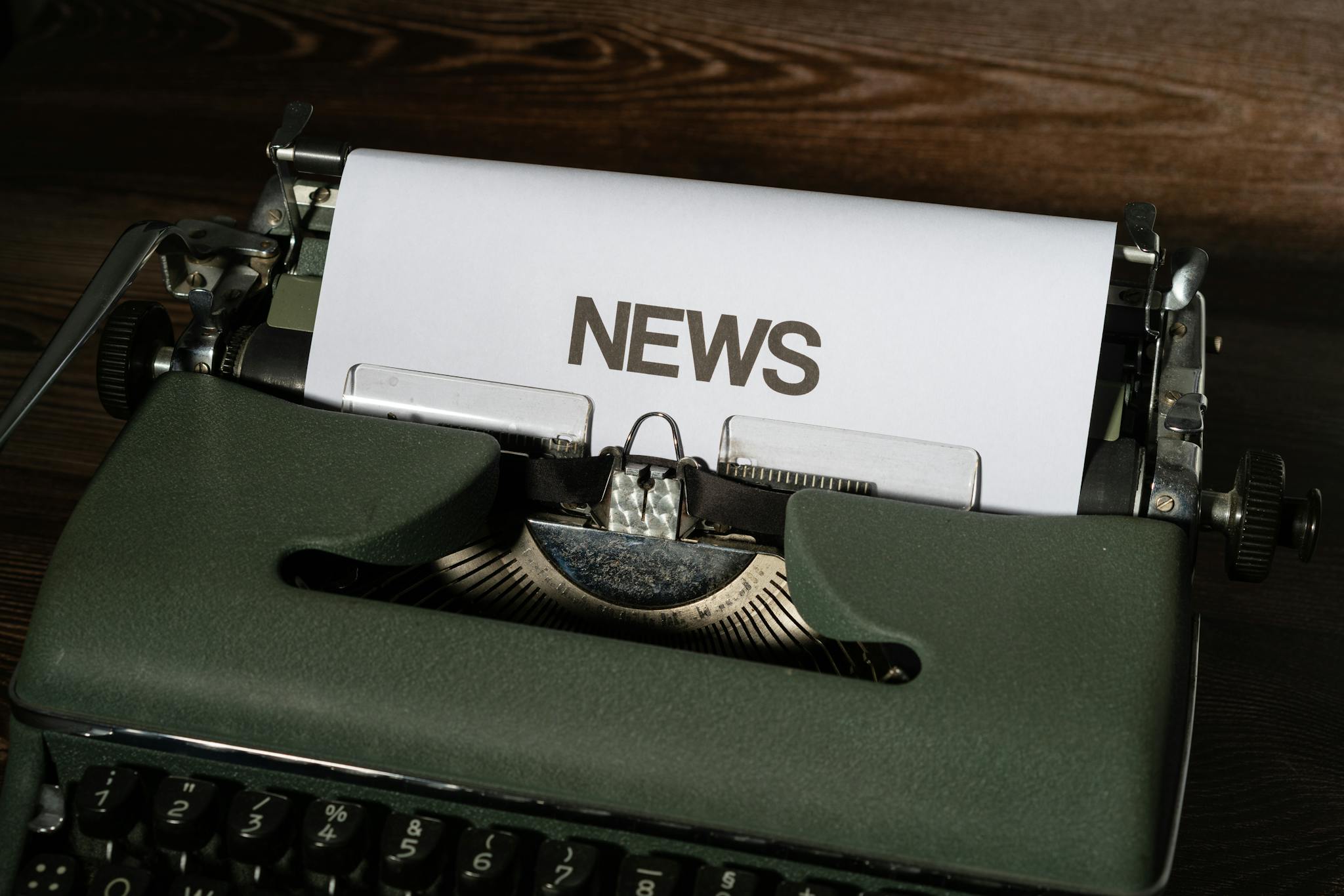 A retro typewriter featuring a 'NEWS' headline typed on white paper against a wooden surface.
