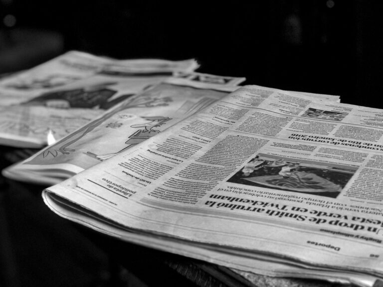 Black and white close-up image of newspapers laid on a table, emphasizing print media.