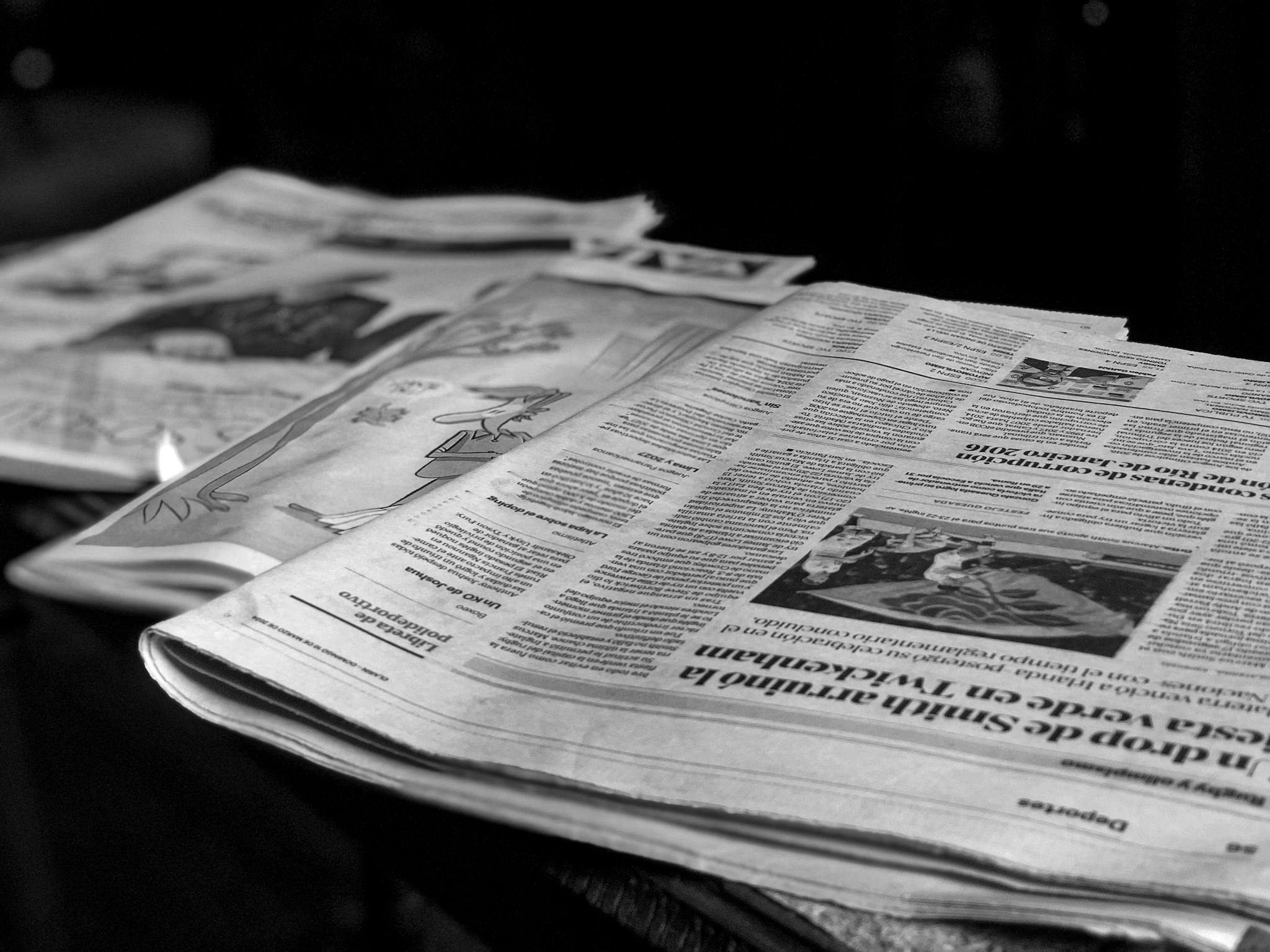 Black and white close-up image of newspapers laid on a table, emphasizing print media.