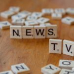 Close-up of Scrabble tiles spelling News and TV on a wooden surface.